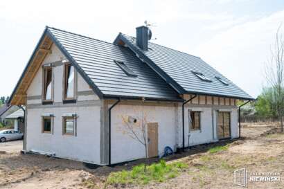Nieotynkowany dom z ciemnym dachem, oknami dachowymi i drewnopodobną stolarką, realizacja w Szczytnie 2025