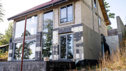 Wysokie okna o ciemnych ramach w ocieplanej ścianie domu w budowie, realizacja w Mrągowie 2023