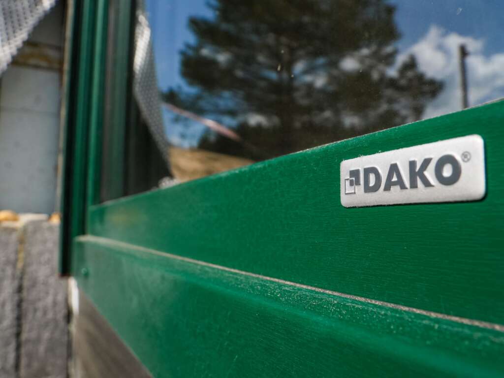 Zbliżenie zielonej ramy z plakietką producenta DAKO i odbiciem drzewa w szybie