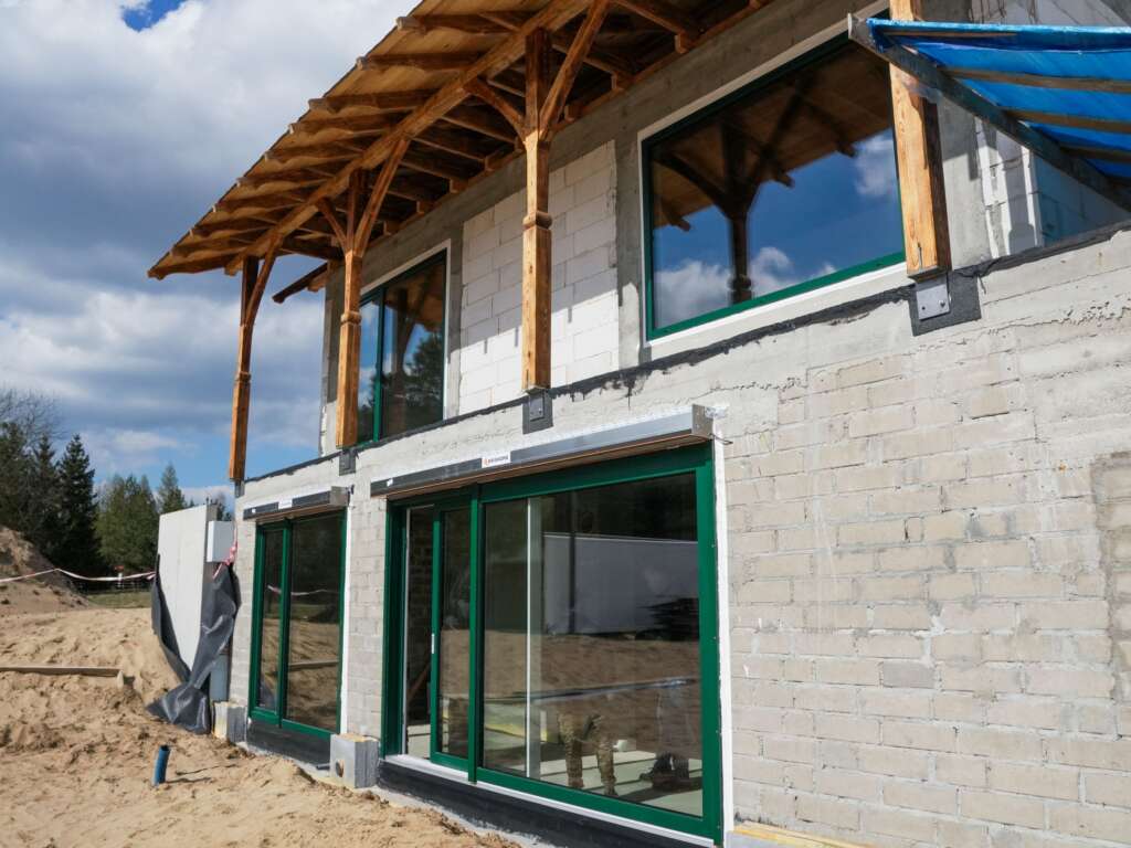 Widok z boku na zielone drzwi tarasowe i okna piętra pod drewnianą konstrukcją zadaszenia