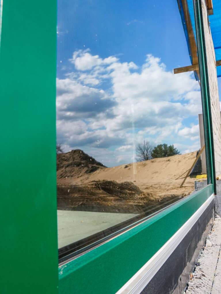 Zbliżenie zielonej ramy i dużej szyby odbijającej niebo z chmurami i plac budowy