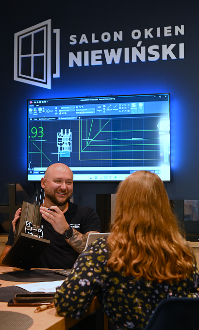 Doradca w salonie Niewiński pokazuje klientce przekrój profilu na tle rysunku technicznego