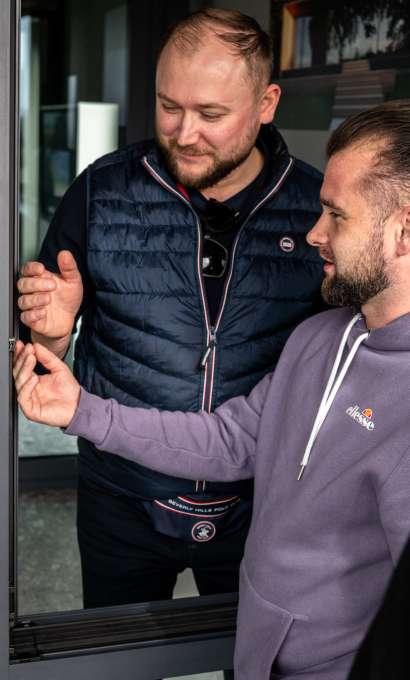 Dwóch mężczyzn ogląda krawędź skrzydła przeszklonych drzwi w szarej ramie