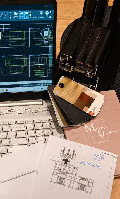 Laptop z rysunkiem technicznym, próbnik kolorów, przekrój profilu i szkic detalu na biurku